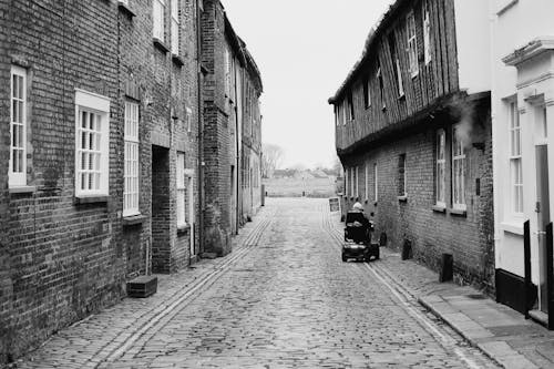 Person in an Electric Wheelchair Riding Down a Cobbled Street Among Old Townhouses