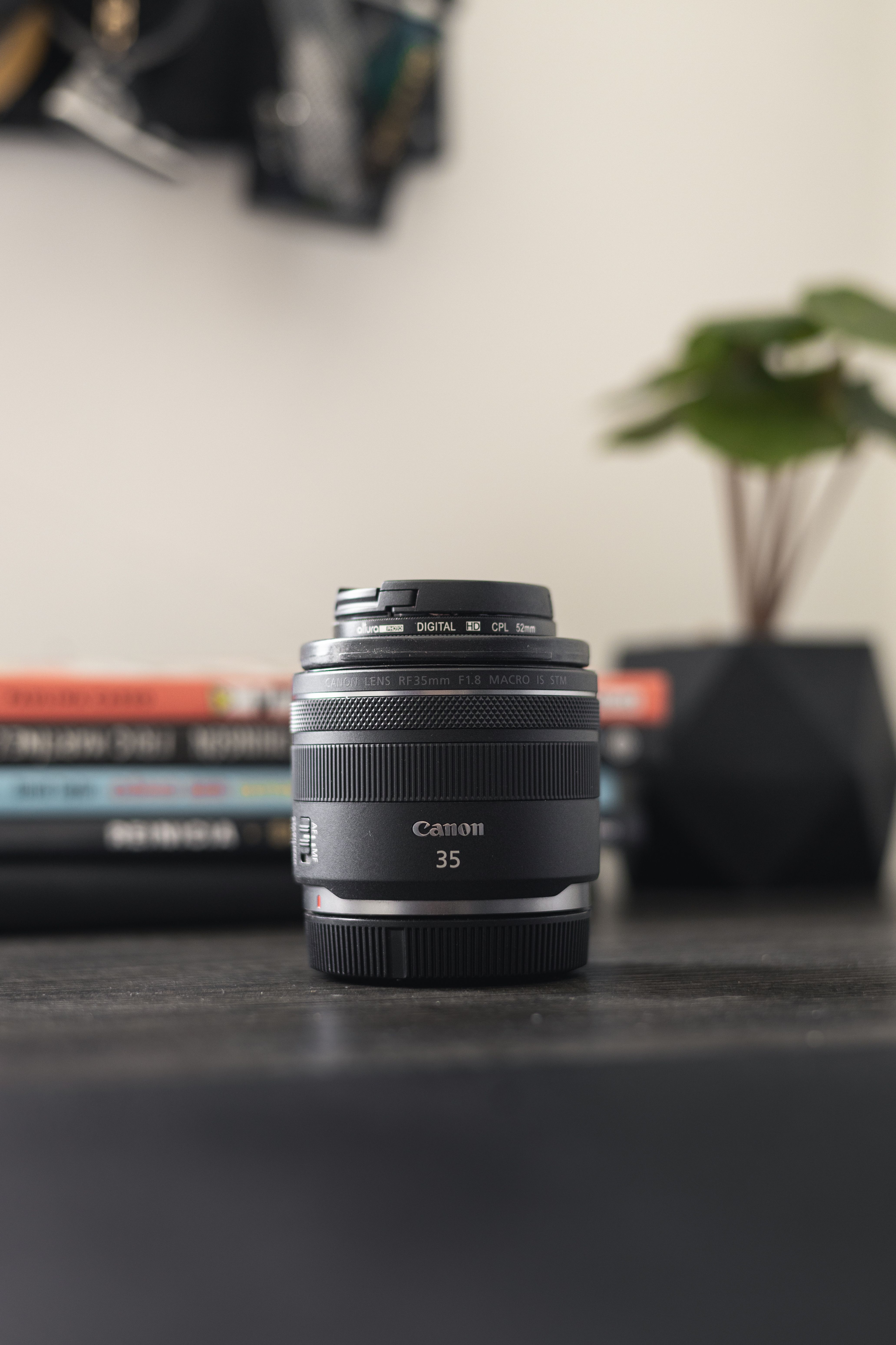 Close-up of a Canon 35mm lens on a table with blurred books in the background.