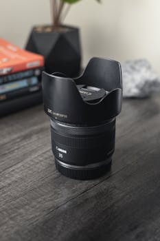 Detailed close-up of a Canon camera lens on a wooden table, surrounded by books.