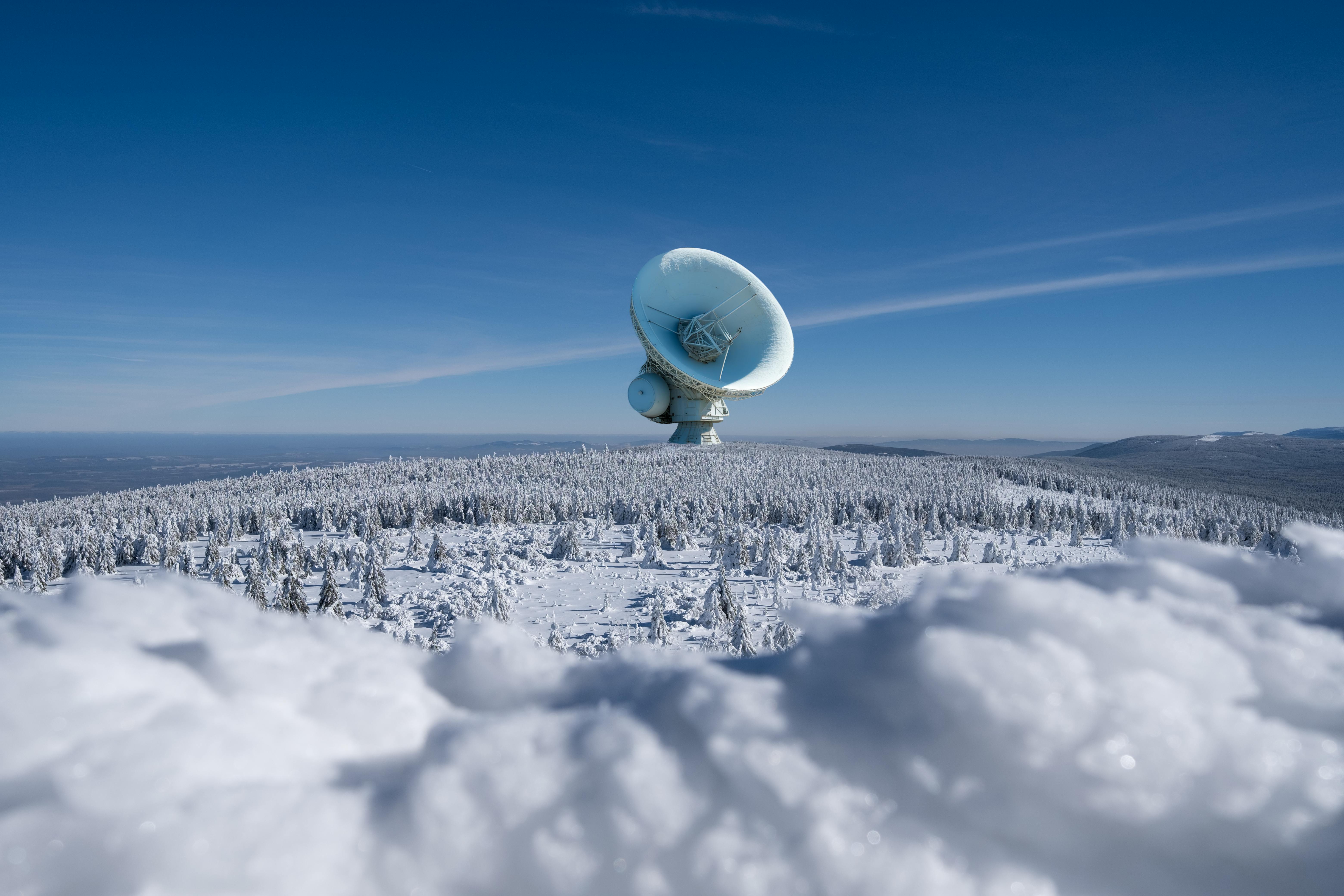 Prescription Goggle Inserts - A large satellite dish observatory surrounded by snowy landscape and winter forest under a clear blue sky.