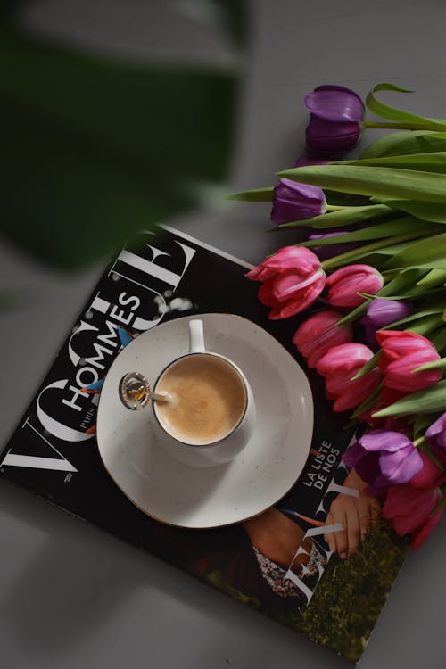A Cup of Coffee Standing on the Vogue Fashion Magazine with a Bunch of Tulips Lying on the Side 