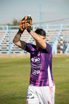 A soccer player in purple kit applauds on a sunny day in Mendoza, Argentina.