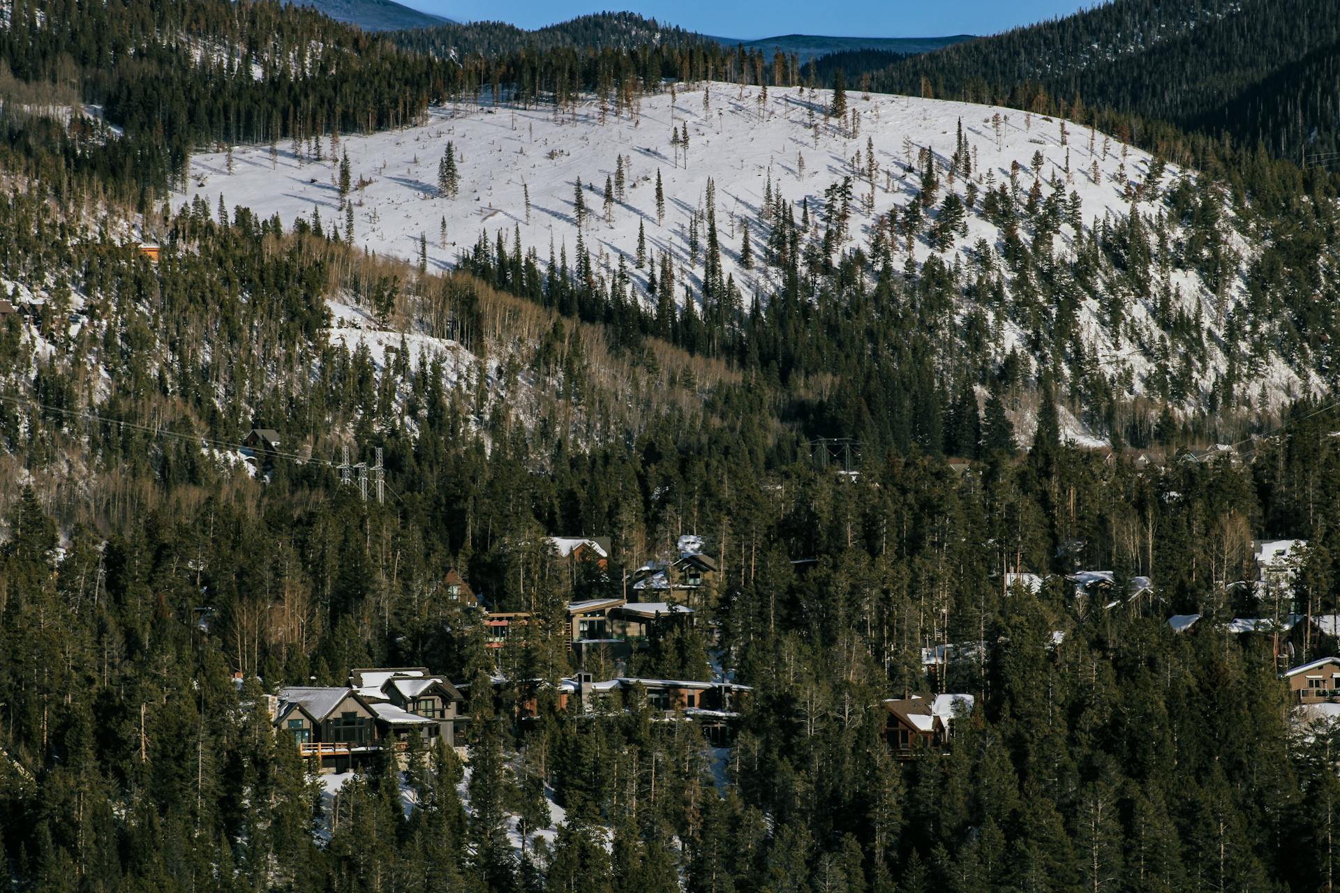 A picturesque winter landscape of snow-covered hills and coniferous forest in Colorado with cabins nestled among trees.