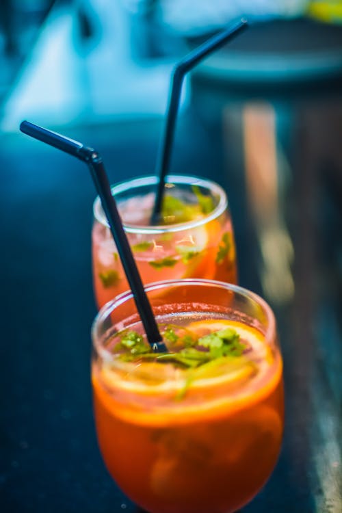 Two Beverages In Footed Glasses With Black Straws