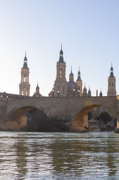 Historic Basilica of Our Lady of the Pillar with stone bridge at sunset in Zaragoza, Spain.
