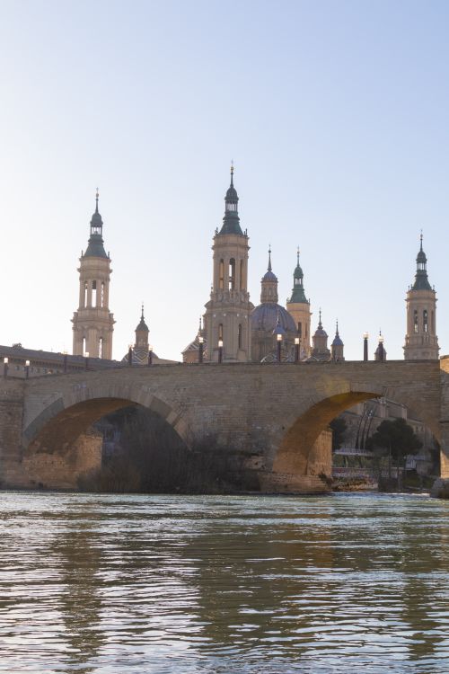 Free Historic Basilica of Our Lady of the Pillar with stone bridge at sunset in Zaragoza, Spain. Stock Photo