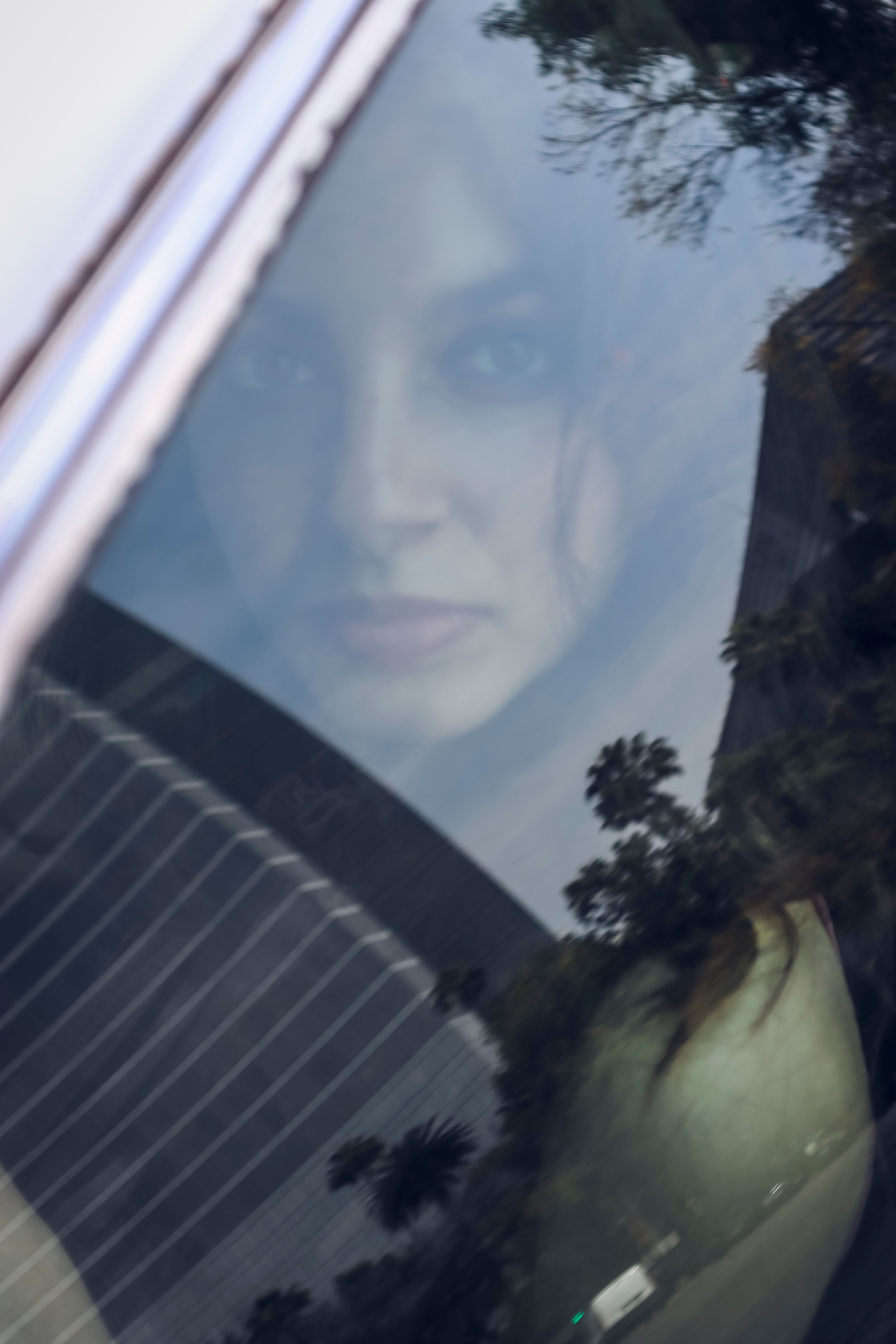 Artistic reflection of a woman's face seen through a car window, capturing urban life themes.