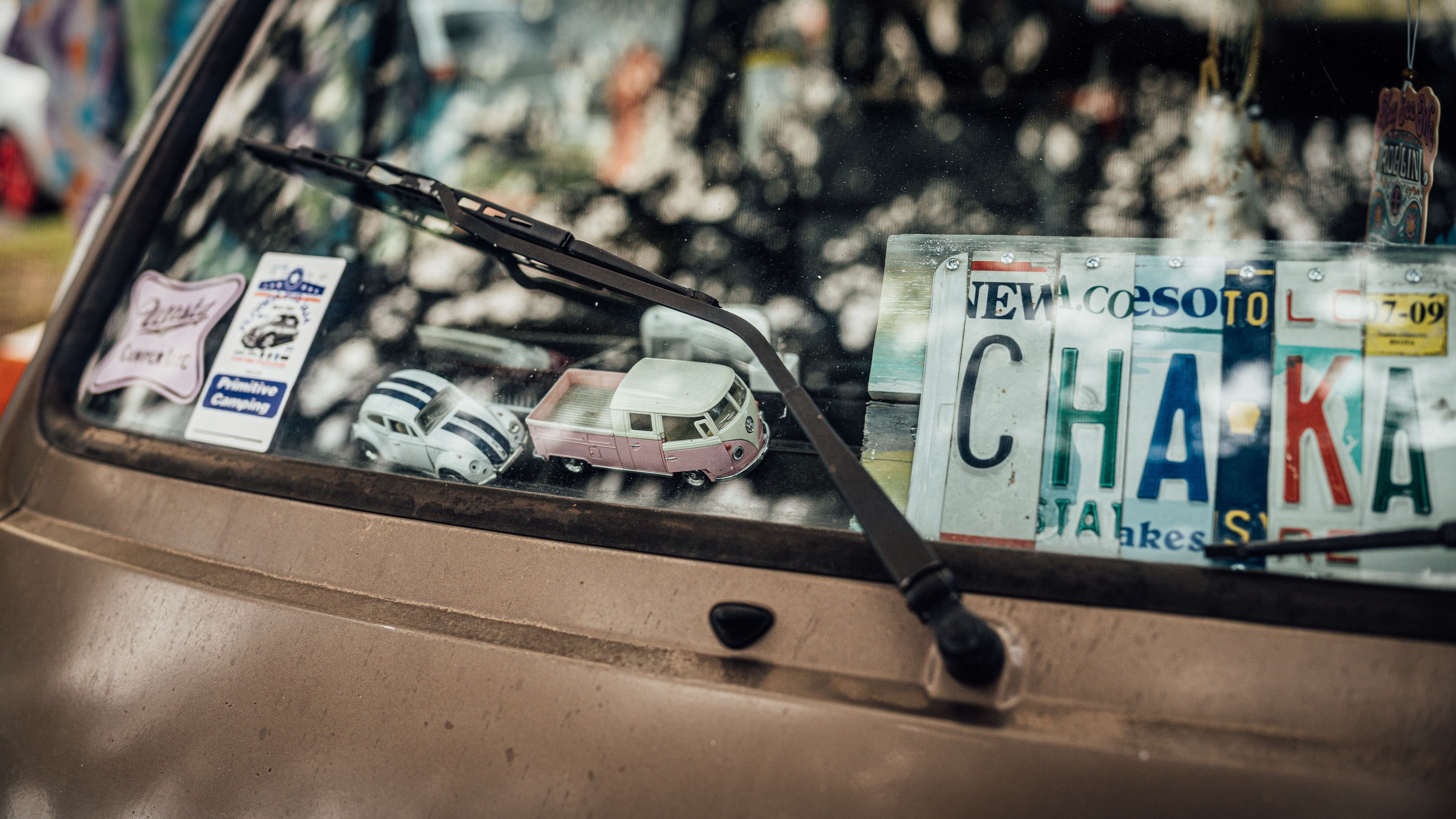 Visão frontal de um carro antigo com itens decorativos e placas de sinalização na moldura do para-brisa, criando uma atmosfera de nostalgia e cultura local.