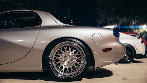 Close-up of a silver luxury car's wheel and side view at night in a parking lot.