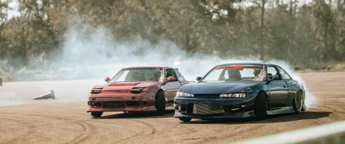 Free Two sports cars drift around a track emitting smoke, showcasing speed and precision. Stock Photo