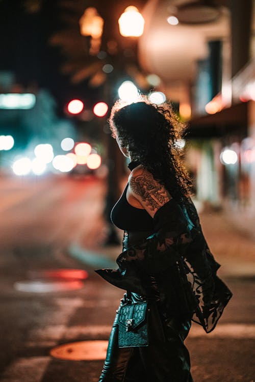A Fashionable Woman on a Sidewalk in City at Night 