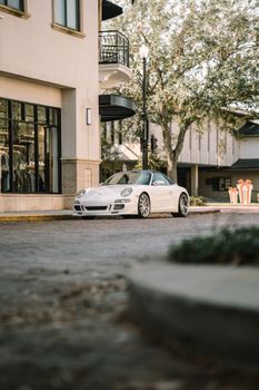 A luxury white sports car parked on an urban street near modern architecture.