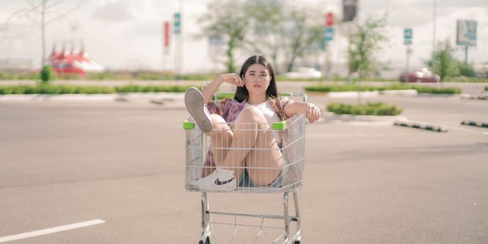 Playful scene of a young woman sitting in a shopping cart outdoors.