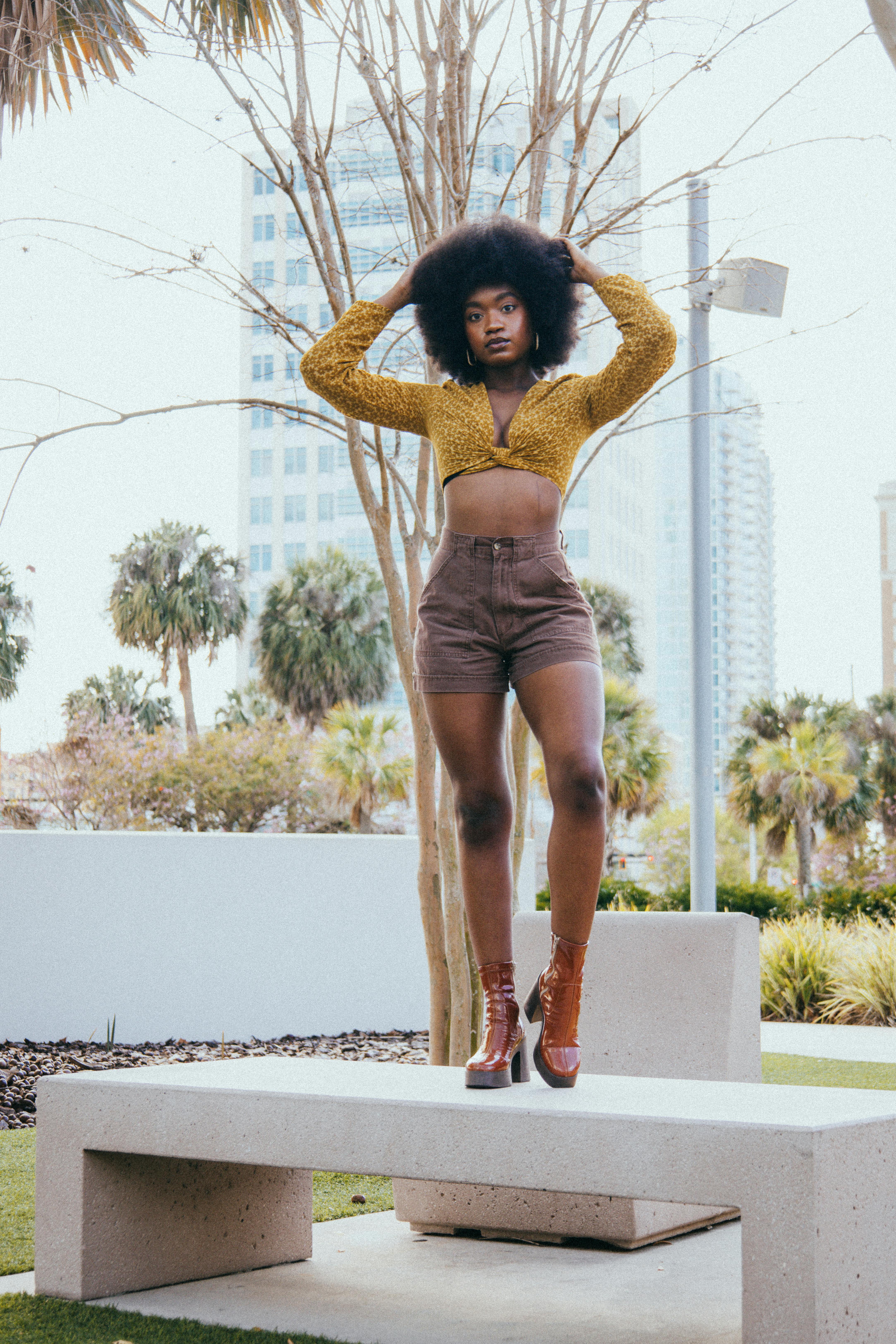 a woman in a yellow top and brown shorts standing on a ledge