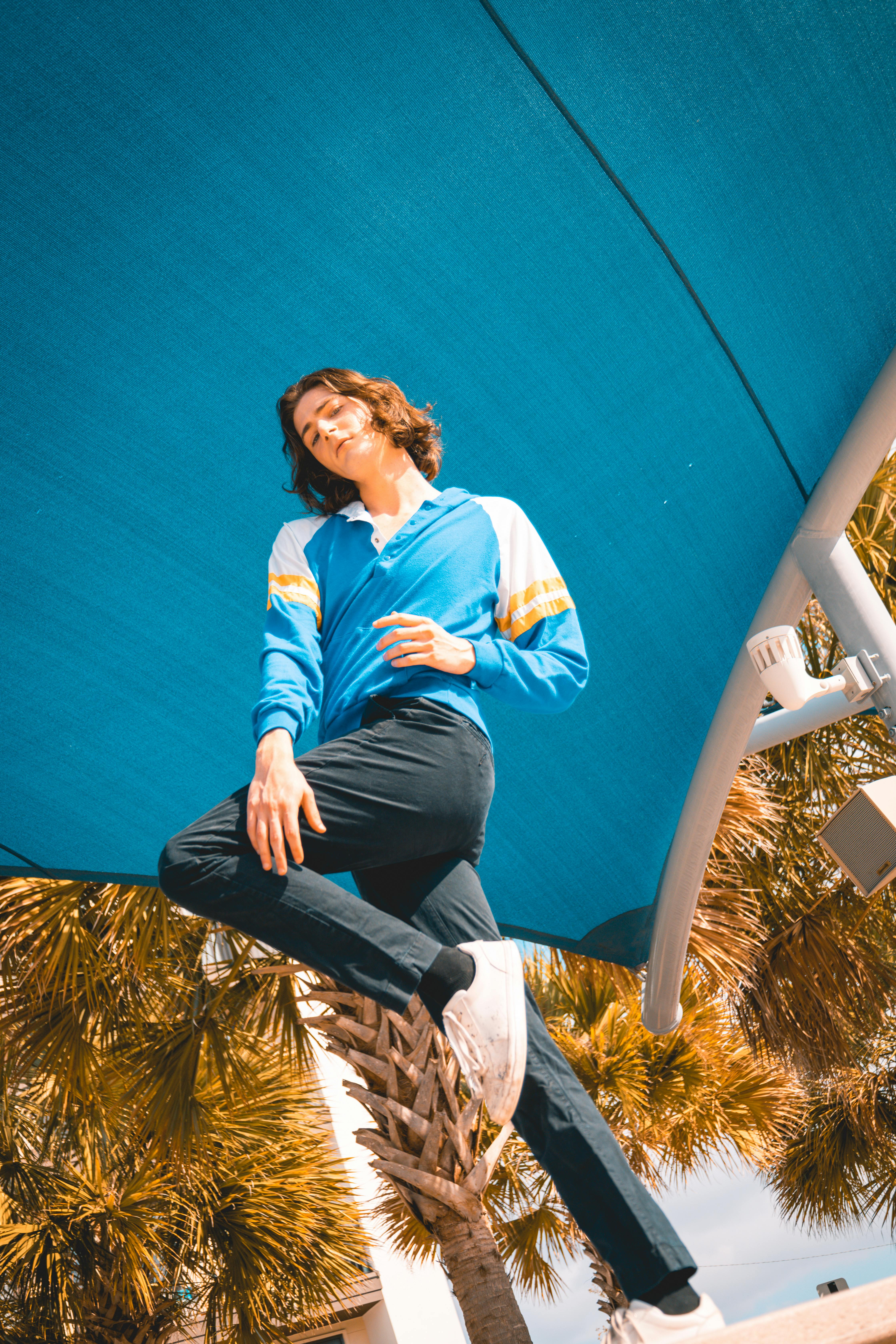 A man in a blue shirt and white pants is jumping on a blue and white umbrella