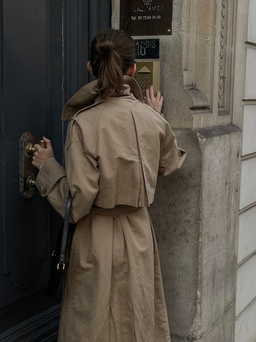 Back View of a Woman in a Trench Coat Opening the Door to a Tenement House 