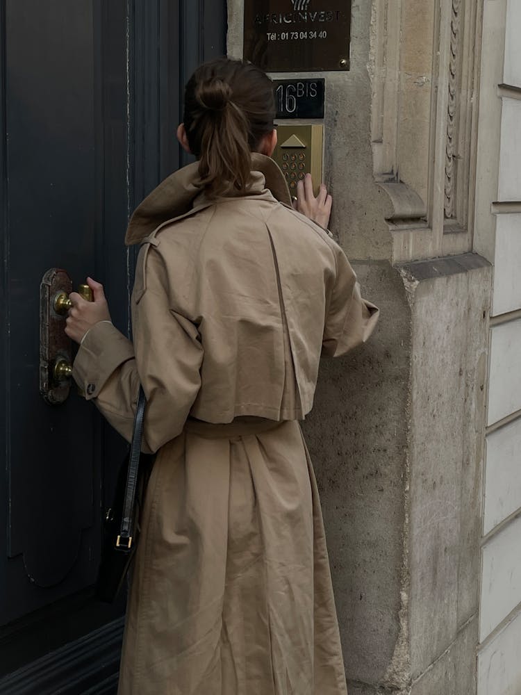 Back View Of A Woman In A Trench Coat Opening The Door To A Tenement House 