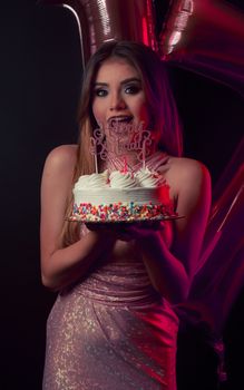 A woman in a pink dress holds a vibrant birthday cake with balloons, creating a joyful party scene.