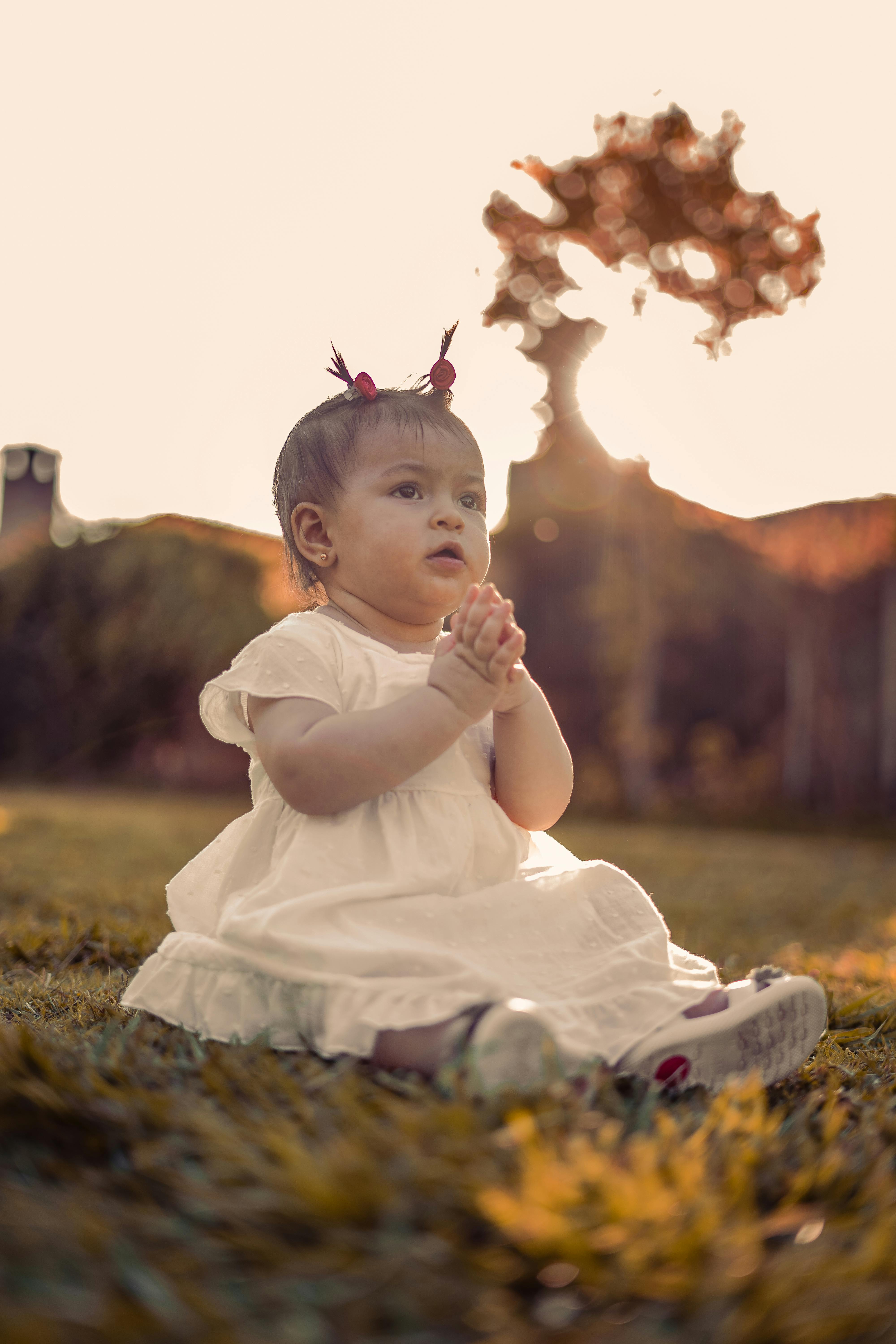 A young girl sits on the grass at sunset, evoking a warm and serene atmosphere.