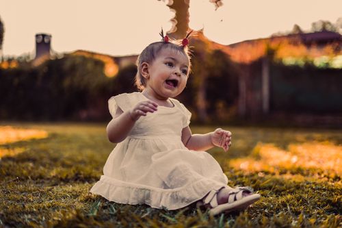 Free A happy baby girl playing on the grass in a park during sunset, enjoying the summer outdoors. Stock Photo
