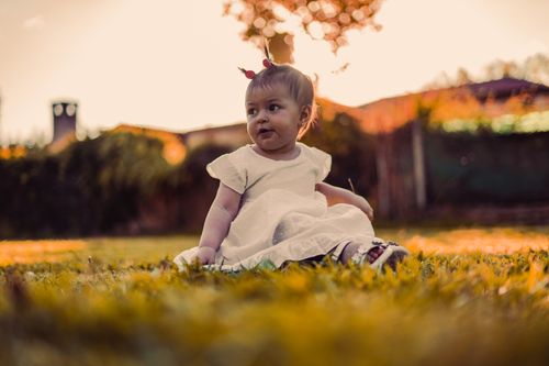 Free Cute young girl in a white dress sitting on grass during a beautiful sunset. Stock Photo