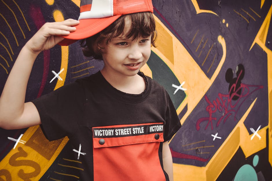 A cheerful child wearing a red cap poses near a vibrant graffiti wall.