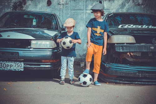 Два мальчика играют в футбольный мяч возле машин