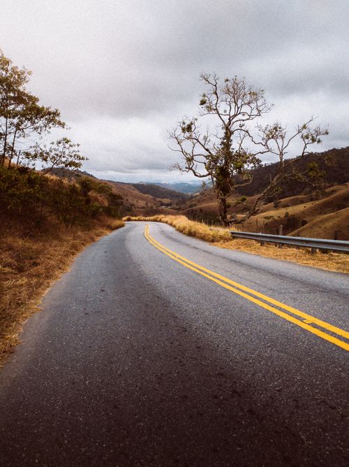 Free Curved asphalt road winding through a tranquil countryside landscape under a cloudy sky. Stock Photo