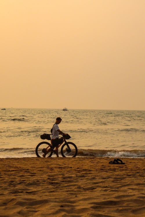 Free A man rides a bicycle along a tranquil beach during a beautiful sunset, reflecting on the sea. Stock Photo