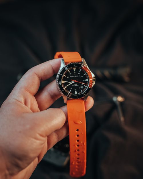 Free Hand holding a luxury Hamilton wristwatch with an orange strap, emphasizing style and elegance. Stock Photo