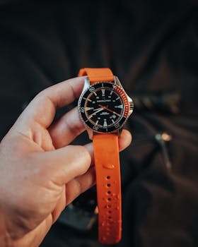 A hand holding a stylish watch with an orange strap, captured in a warm and classic tone.