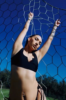 Confident woman in swimsuit holds net outdoors under a clear blue sky, exuding strength and style.