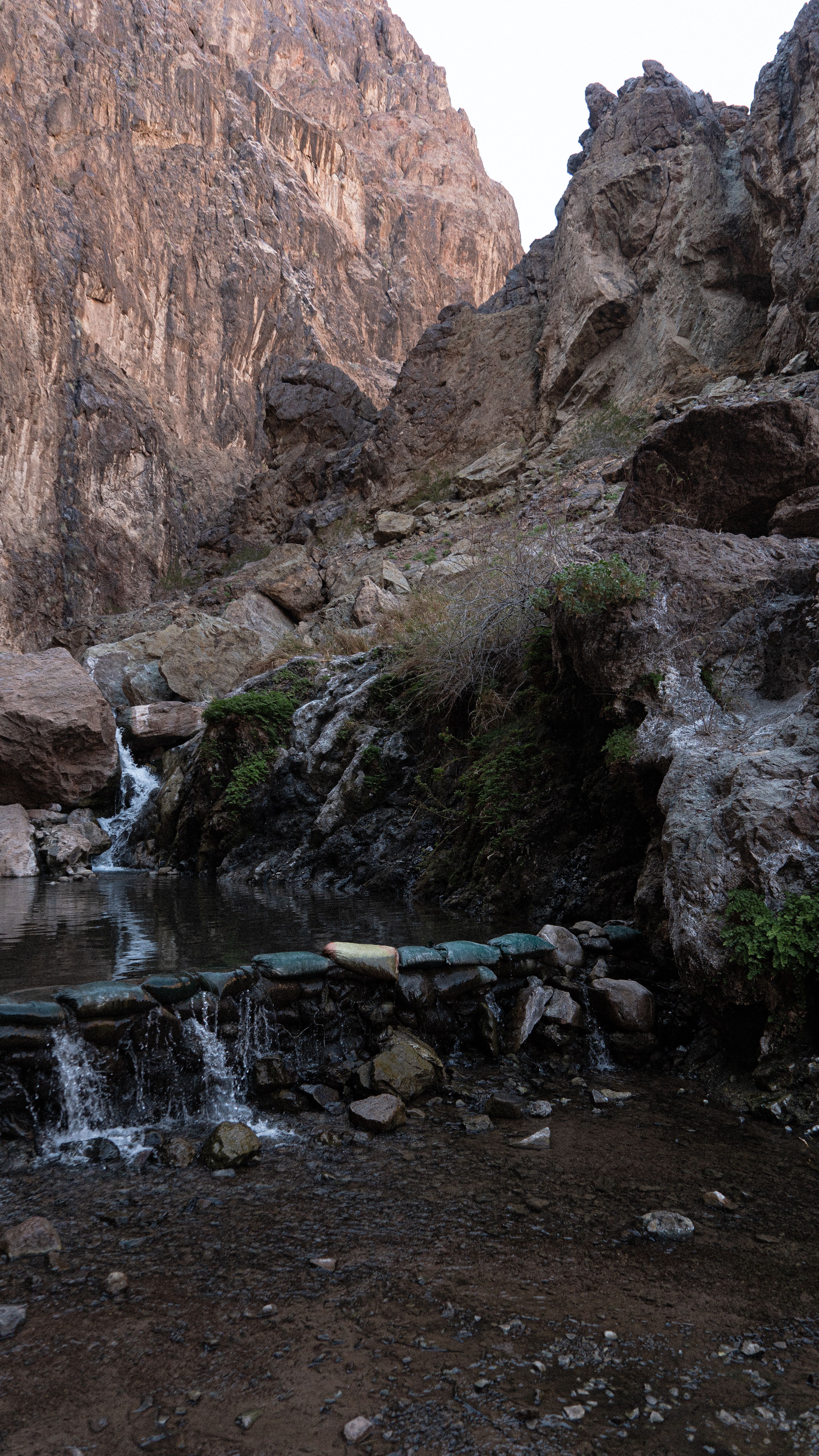 A tranquil waterfall flowing through rocky mountain terrain with greenery, offering a serene natural view.