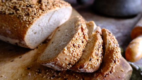 Sliced sesame bread on a rustic board with flour in vintage pot, perfect for bakery and food photography.