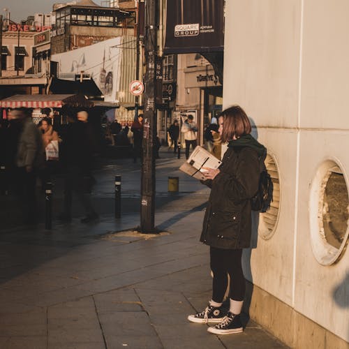 Woman Reading on Sidewalk in Town