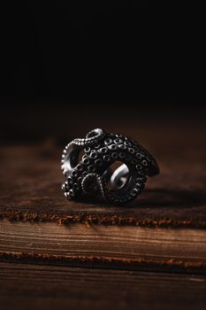 Close-up of a metal octopus tentacle ring displayed on wood, highlighting intricate design.