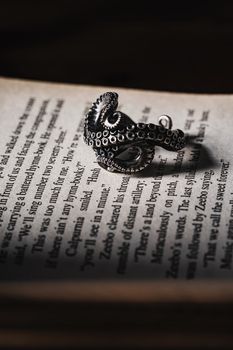 A detailed silver octopus ring rests on the open pages of a book, casting dramatic shadows.