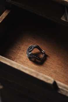 A detailed view of a unique octopus-shaped ring placed inside a wooden drawer under soft lighting.