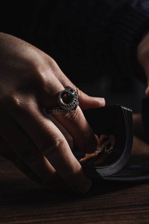 Free A close-up of a hand wearing a silver ring, elegantly holding cards in dramatic lighting. Stock Photo