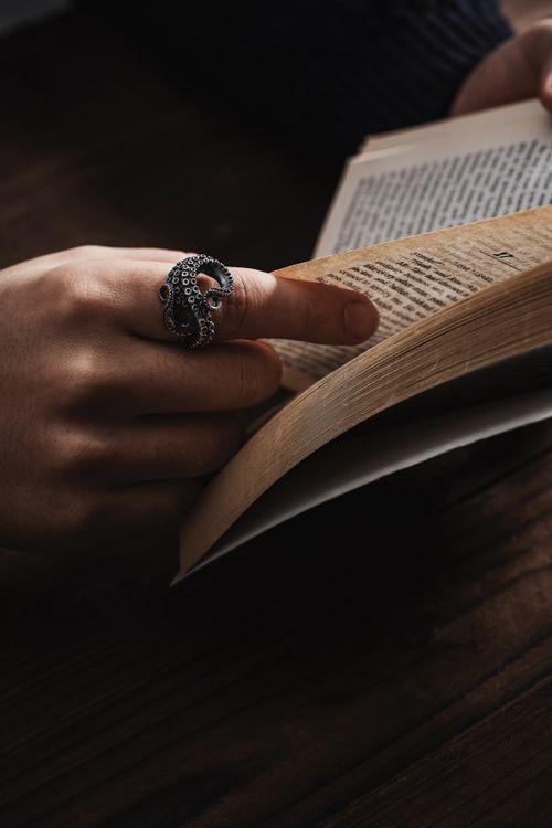 Free Close-up of a hand with a silver octopus ring turning pages of a book in warm lighting. Stock Photo