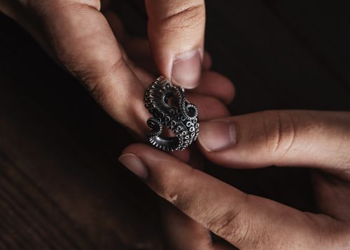 Free Detailed shot of hands holding an octopus-shaped silver ring on a wooden surface. Stock Photo