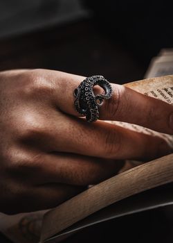 Closeup of a hand wearing an octopus-shaped silver ring holding a book.