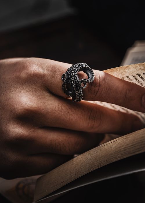 Free Closeup of a hand wearing an octopus-shaped silver ring holding a book. Stock Photo