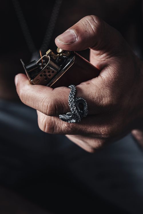 Free Close-up of a hand holding a lighter, adorned with a unique octopus tentacle ring. Stock Photo
