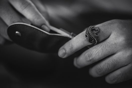 Black and white close-up of a hand wearing an octopus ring and holding a knife.