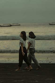 Two women walking along a Bali beach at sunset, capturing friendship and serenity.