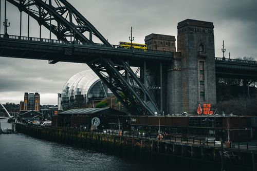 Free Yellow bus crossing iconic urban bridge under overcast skies by the river. Stock Photo