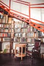 一个舒适的图书馆角落，设有书架、木椅和红色楼梯，呈现出现代室内风格