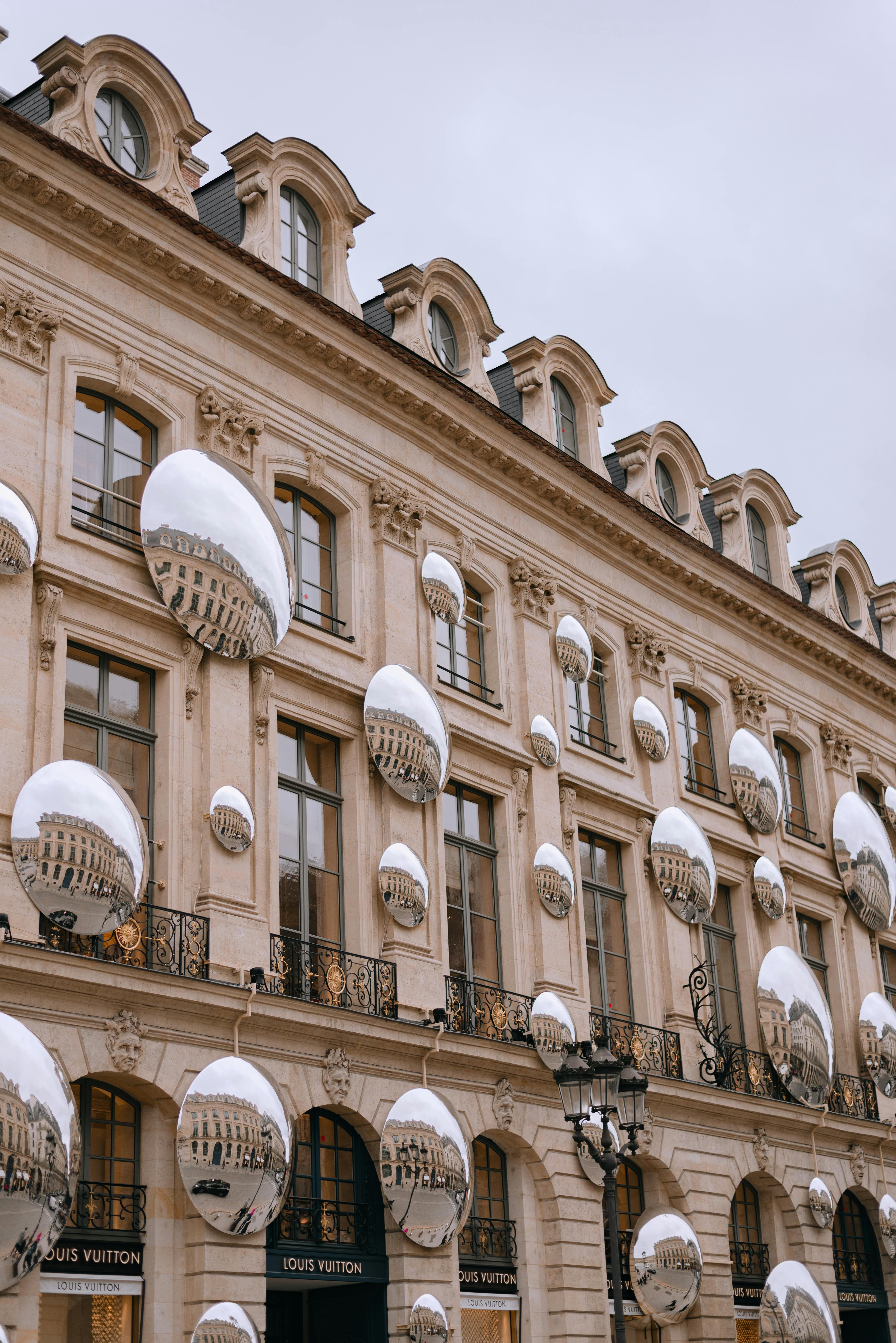 Historic Parisian architecture adorned with reflective modern art spheres on a cloudy day.