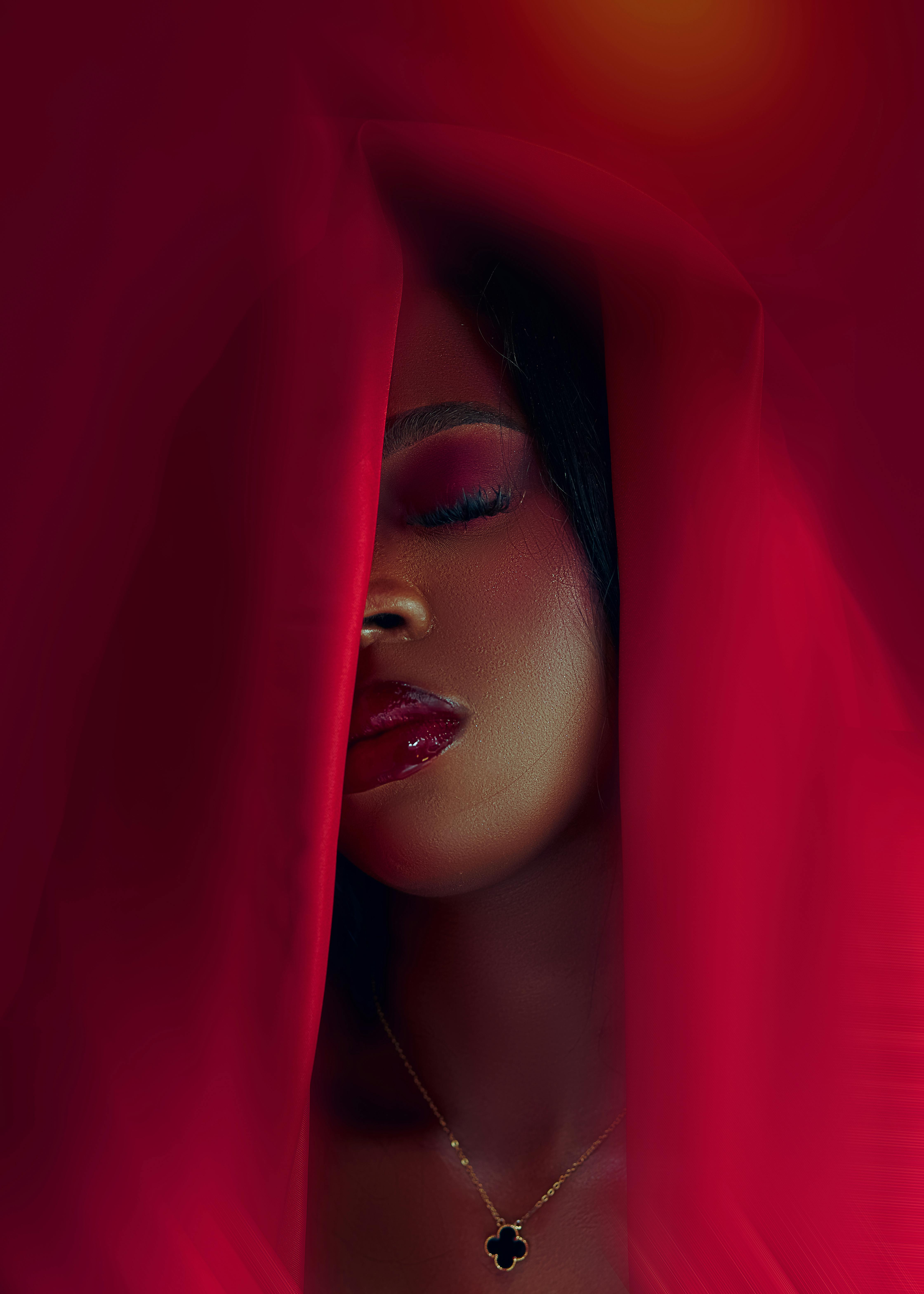 Close-up portrait of a woman with vibrant makeup, wrapped in red fabric, exuding elegance and style.